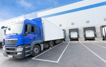 Big distribution warehouse with gates for loads and blue truck Big distribution warehouse with gates for loads and blue truck