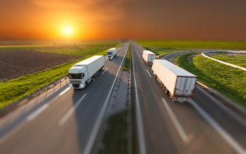 Many white trucks driving towards the sun. Fast blurred motion driving on the freeway in tilt shift technique. Freight scene on the motorway near Belgrade, Serbia.